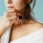 Kobieta w szlafroku nakłada serum na twarz w ramach pielęgnacji